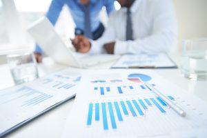 Documents with chart and graph and pen on background of two employees working